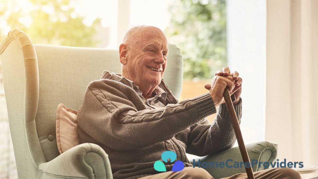 An elderly man visibly smiling as he sits comfortably on a sofa