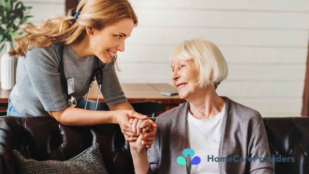 A nurse warmly holding hands with an elderly woman, both smiling