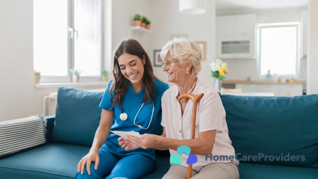 A nurse in a blue uniform reviews a document with an elderly woman holding a cane