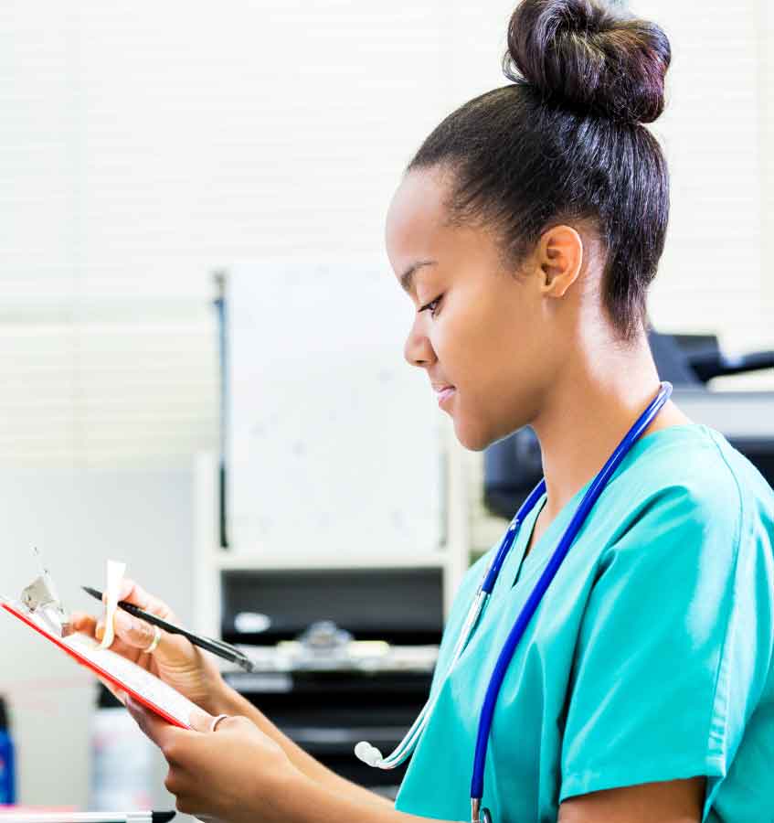 A nurse seated at a workstation, focused on filling out patient records.