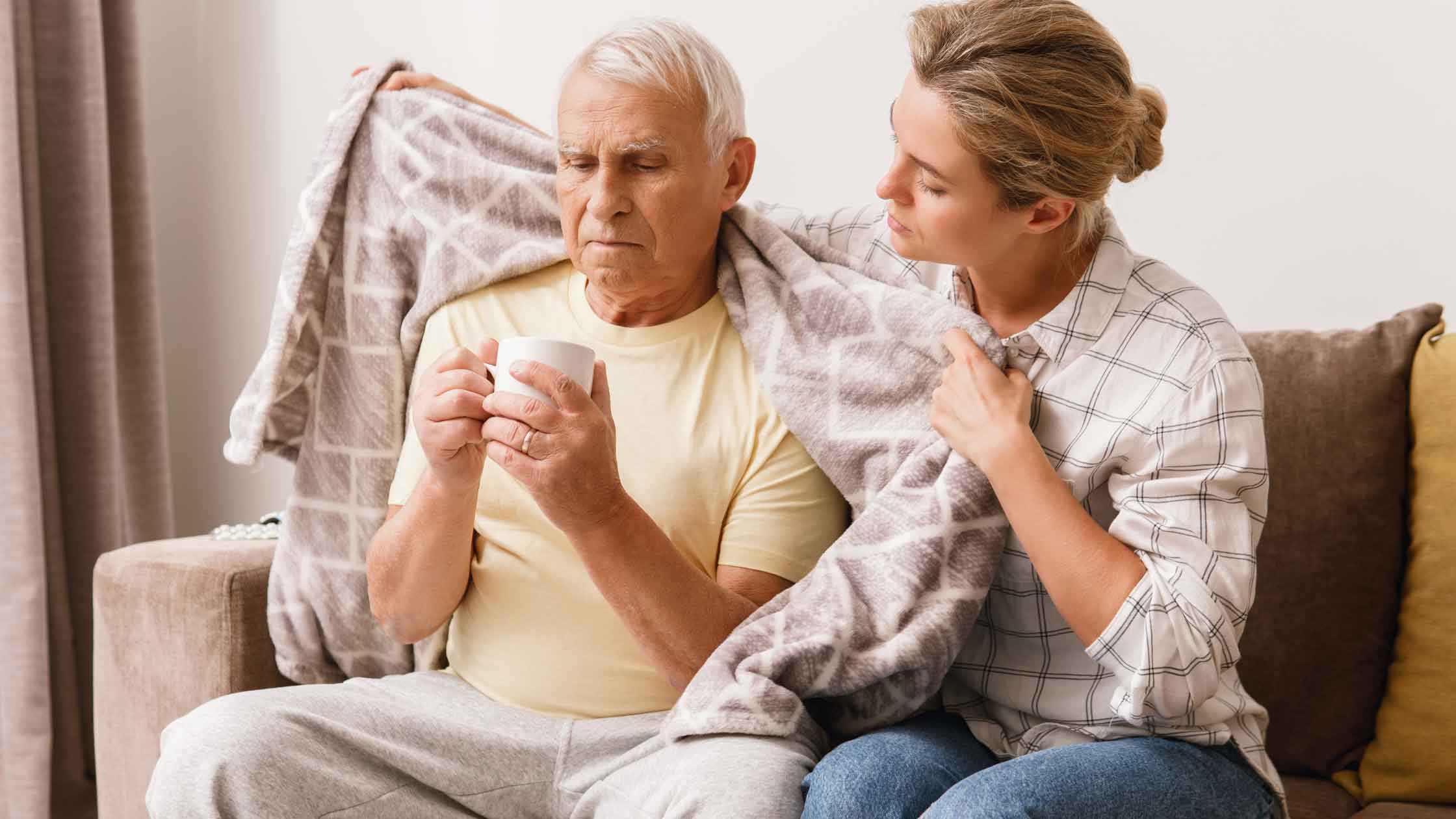A caregiver helping an older adult get comfortable on a sofa