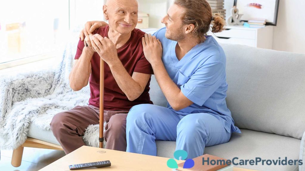 Caregiver sitting beside an elderly man on a sofa