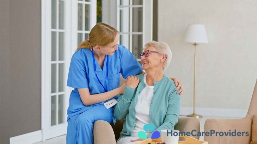 A smiling nurse sitting beside an elderly woman at home, offering companionship