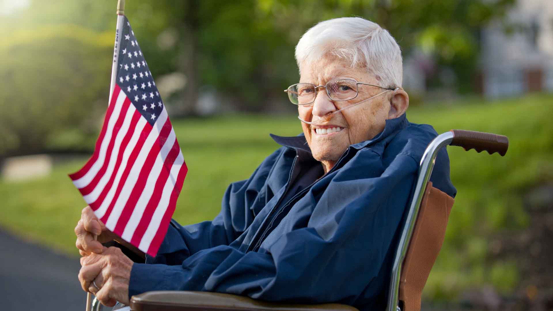 An elderly man in a wheelchair holding the American flag 
