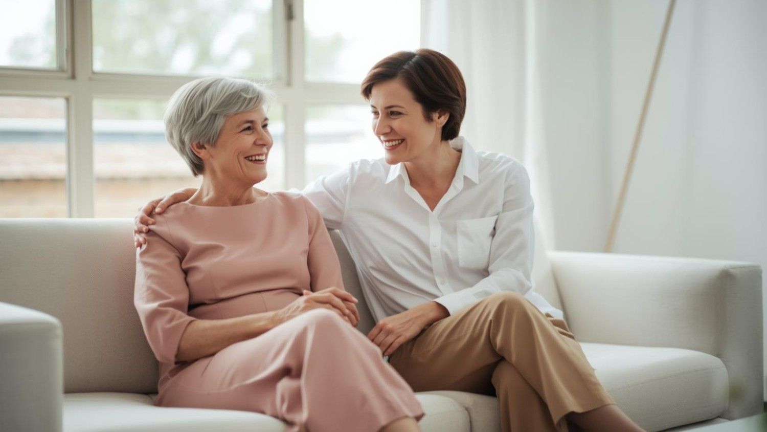 A senior woman and her daughter engaged in a warm and joyful conversation on a couch.